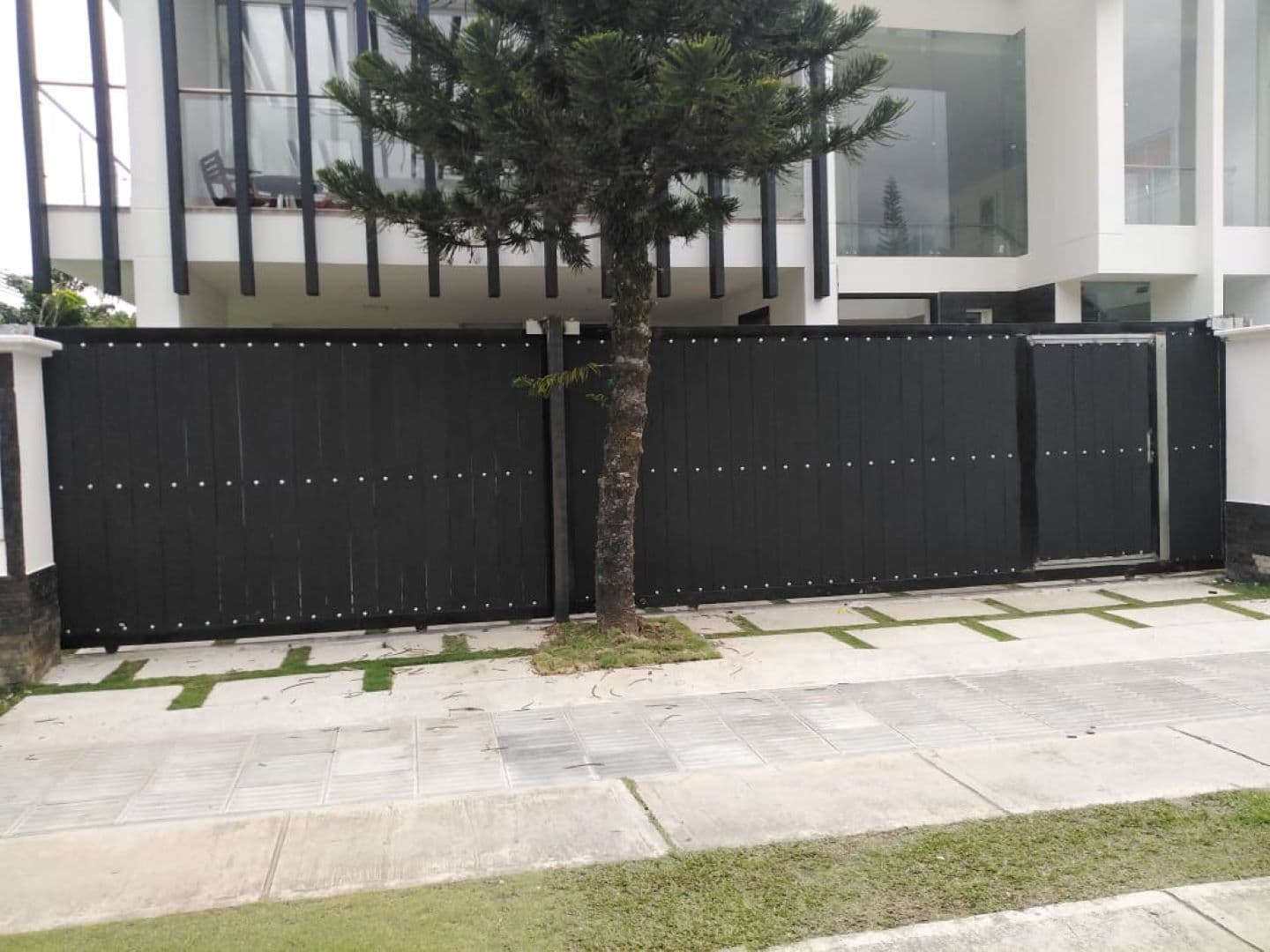 Portón corredizo residencial en panel negro con puerta peatonal